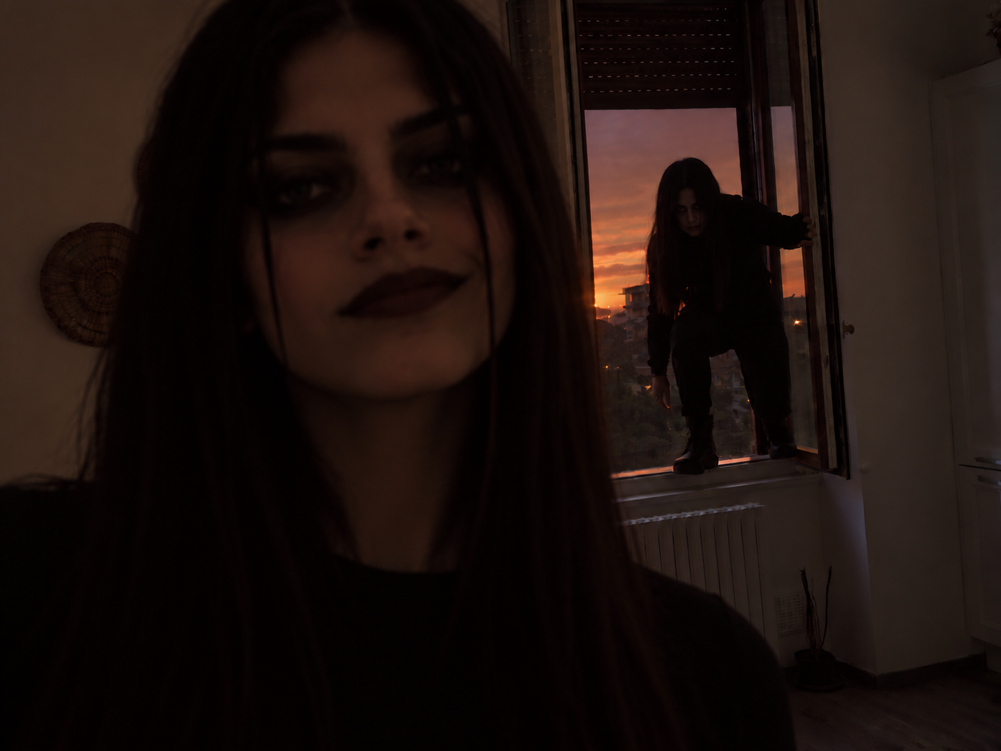 Two girls, very pale, black make up, wearing black clothes. One is standing inside a kitchen, the other is on the window about to break in.